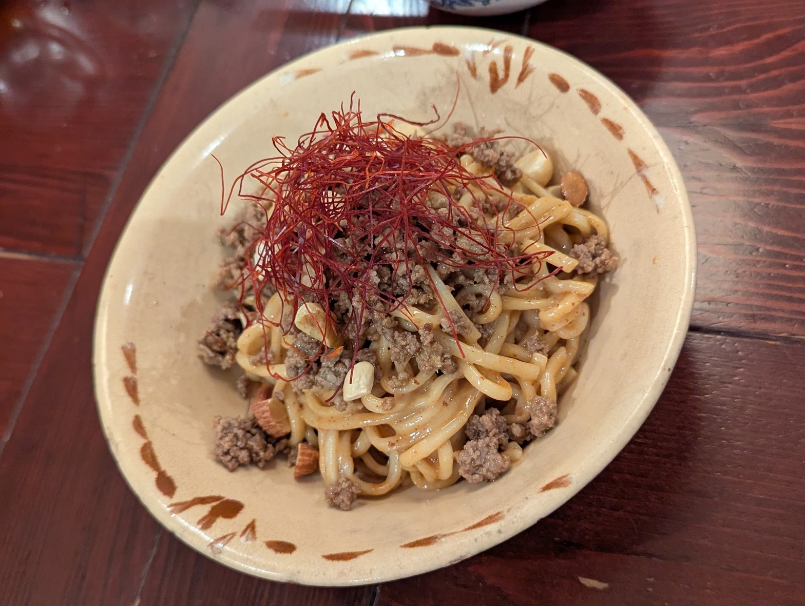 白い丸皿に盛られた和え麺、挽き肉と赤い糸唐辛子が乗った陶器の鉢
